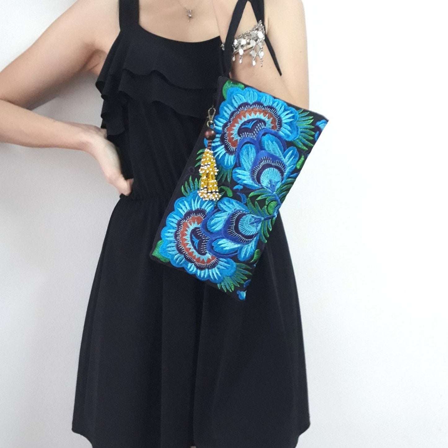 A model wearing an elegant wristlet bag with blue flower embroidery and wrist strap in her hand.