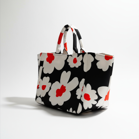 Shopper Bag Flower Bomb in black with bold white daisies and red accents, angled view with handles.
