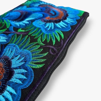 Close-up of a detailed blue flower embroidered wristlet bag with green leaves on black fabric.