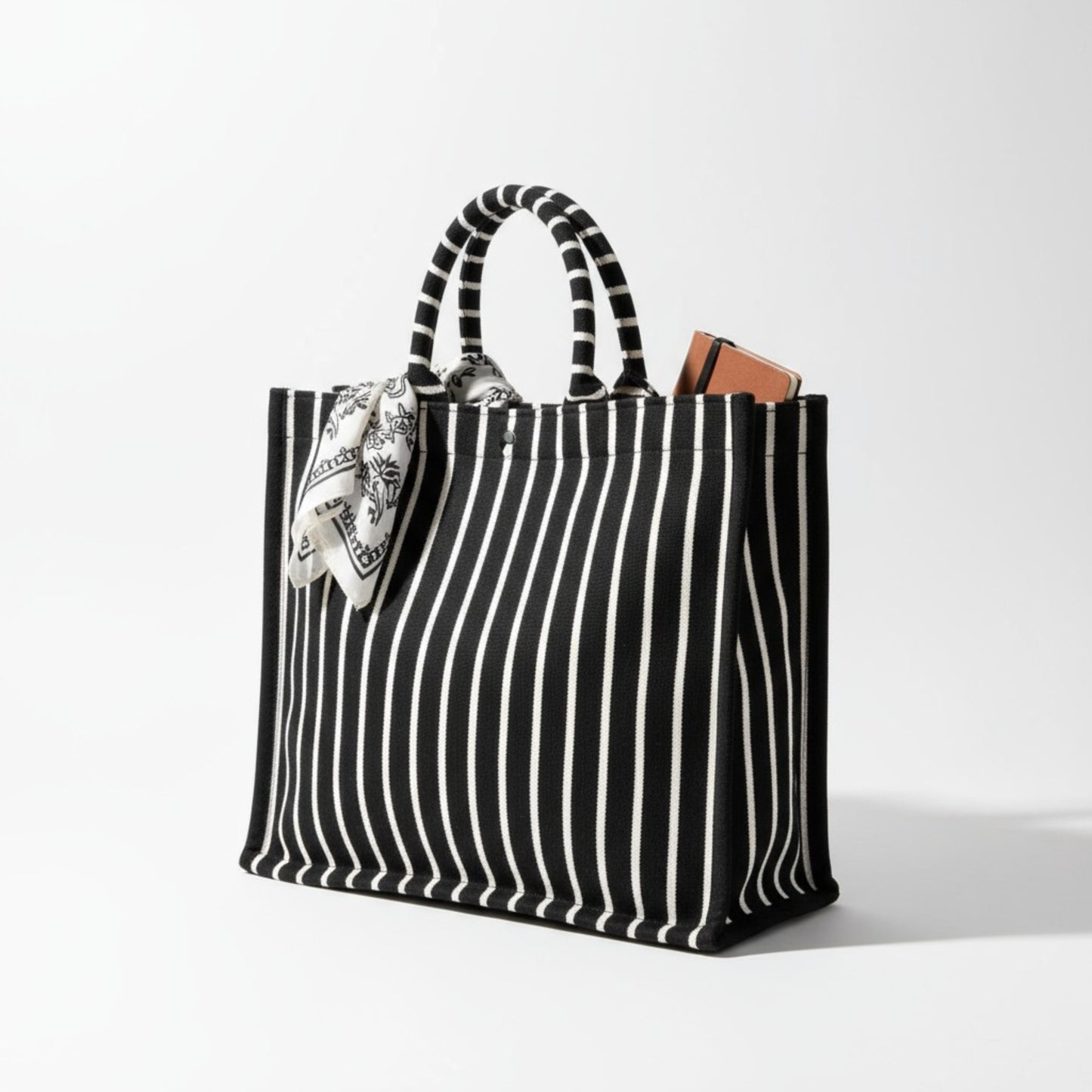 A large black and grey striped tote bag with a notebook and a scarf tied to its handle.