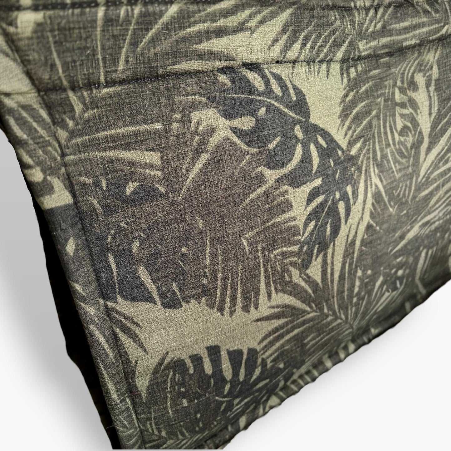 Close-up of a light khaki green textured tote with brown, black monstera and palm leaf patterns.