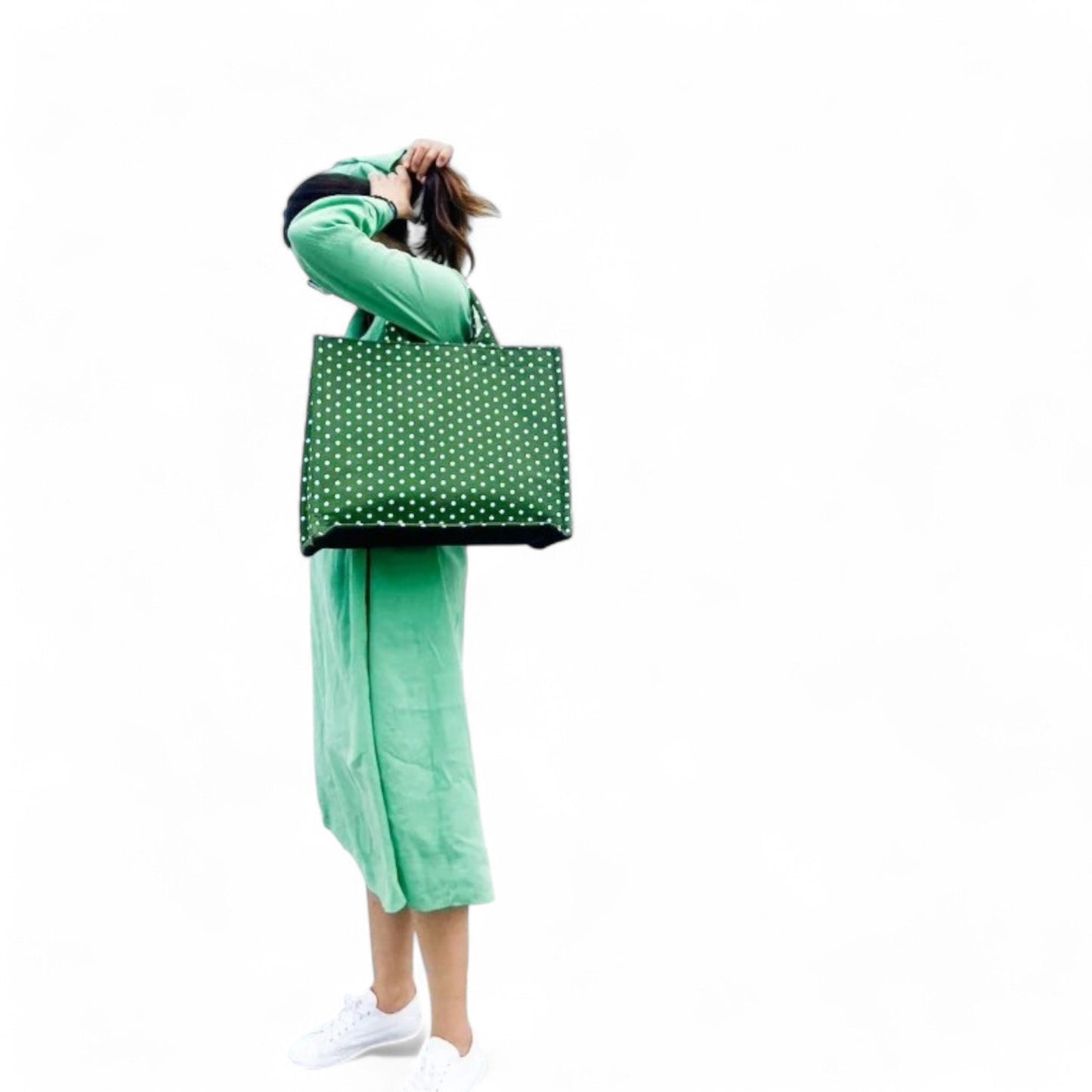 A model wearing a green tote bag with small white polka dots on her shoulder.
