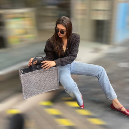 A woman sits on a bench, holding a book and a tote bag in an urban setting.