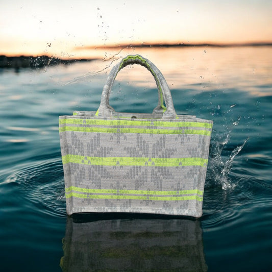 A tote bag with neon green stripes on light grey jacquard fabric on top of a pool of dark blue water. 