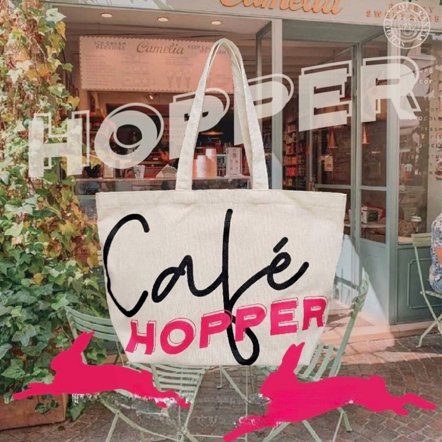 An oversized canvas Café Hopper tote is showcased in front of a café. setting.