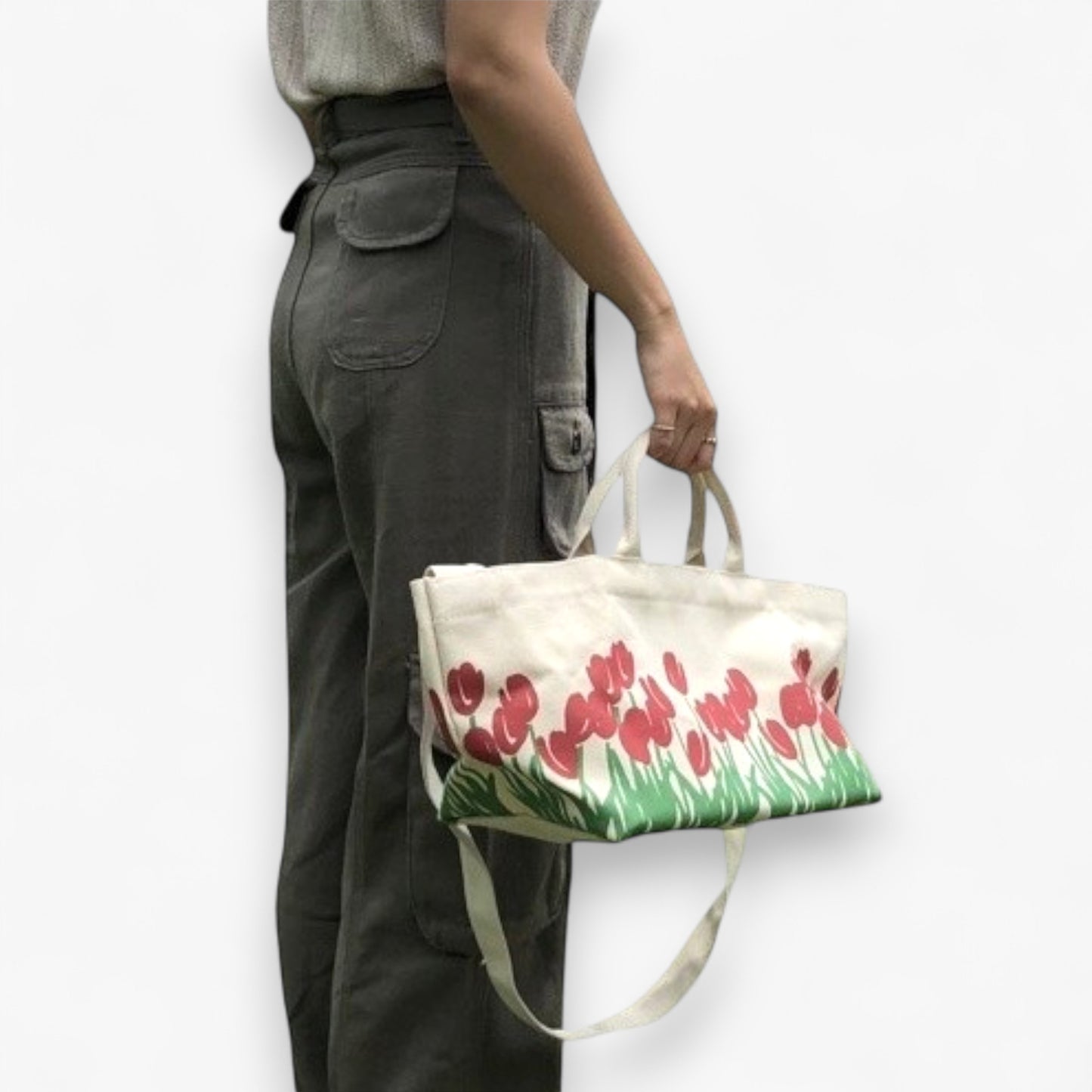 A person holding the top handles of a tote bag with red tulip prints and a shoulder strap.