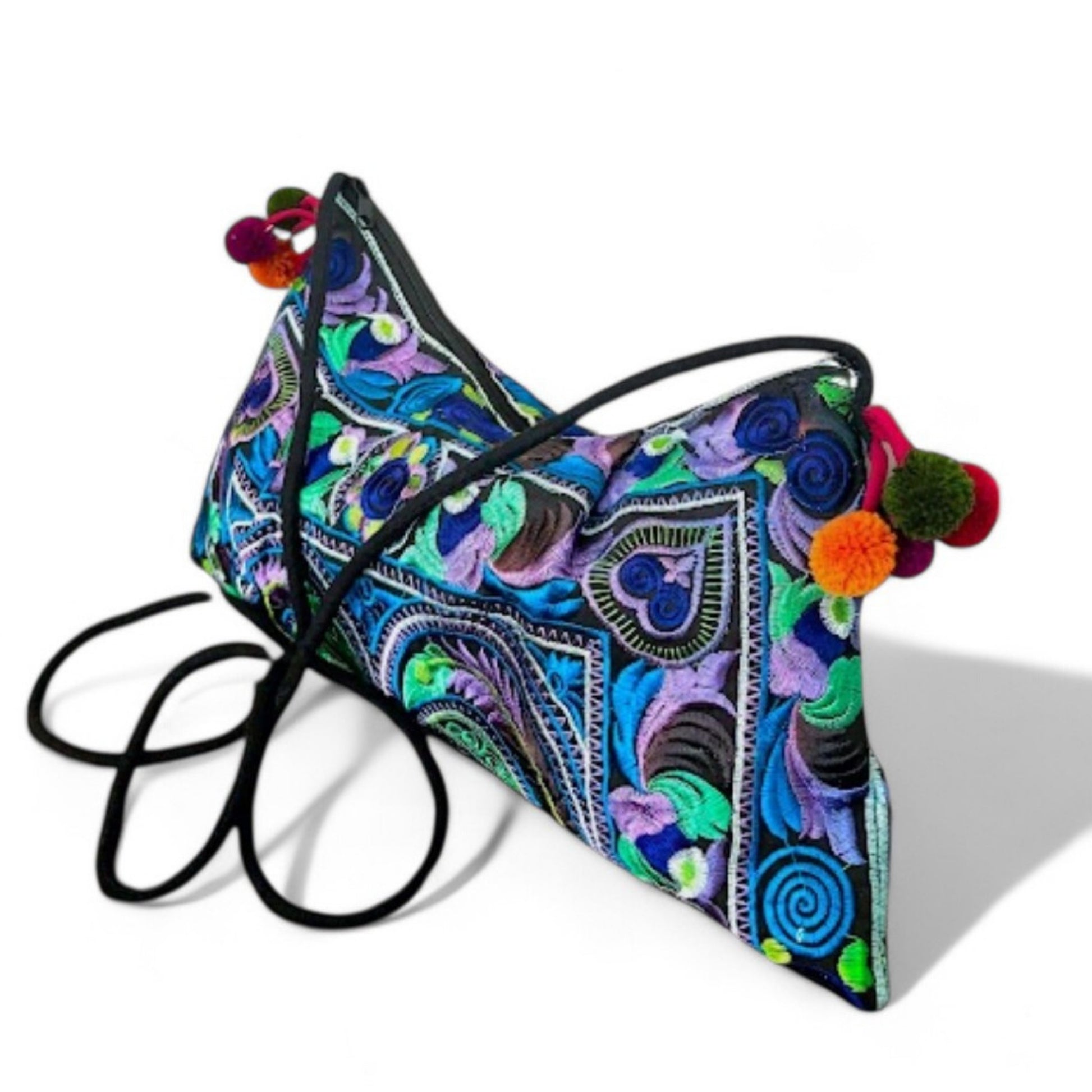 Angled close-up view of a blue multi coloured embroidered crossbody bag with colourful mini pompom charms.