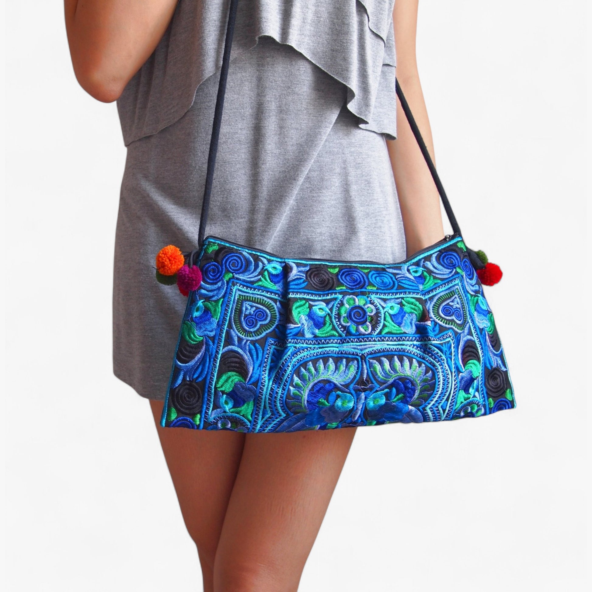 Model wearing a blue embroidered bag with a floral pattern and colourful pom-pom charms.