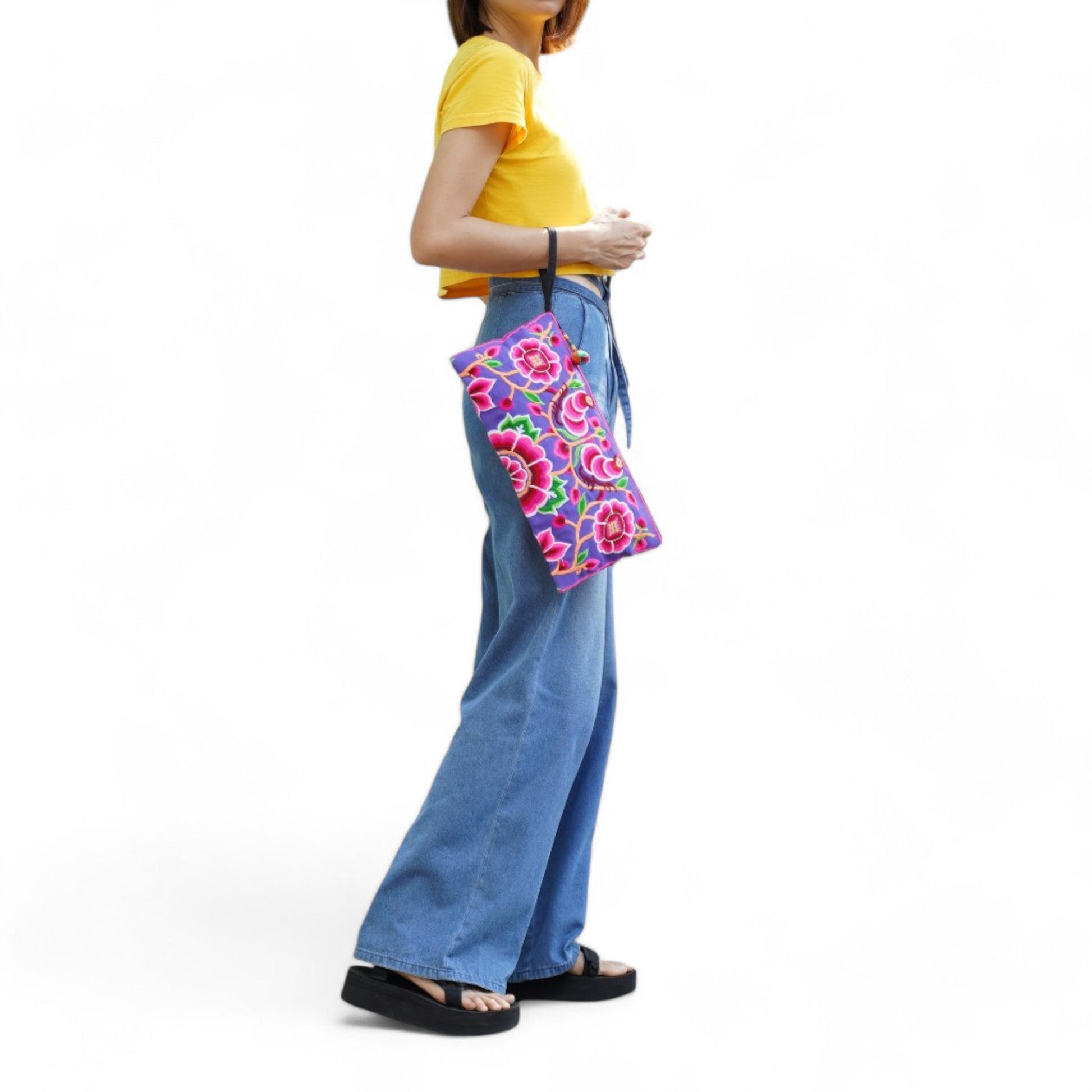 A woman wearing a casual outfit with a Hmong embroidered peony clutch bag on her wrist.