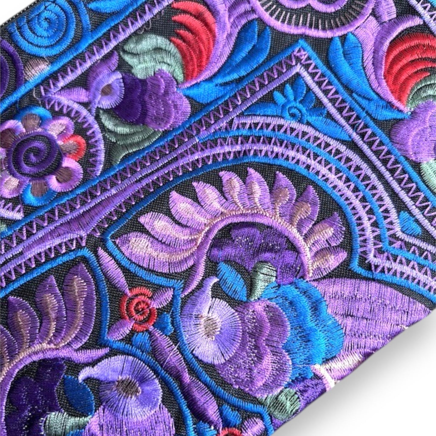 Close-up of a delicate embroidered fabric with bird and floral patterns in purple, blue, and red.