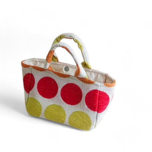A small handmade tote bag with vibrant red, green, and orange dots on beige fabric and light lining.