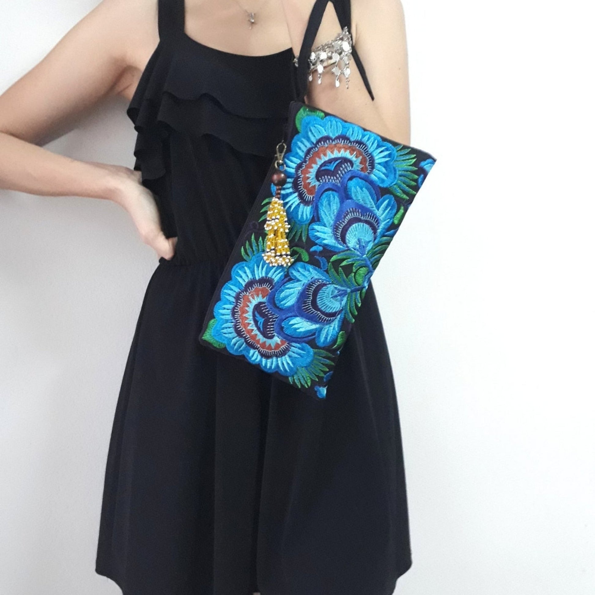 A model wearing an elegant wristlet bag with blue flower embroidery and wrist strap in her hand.
