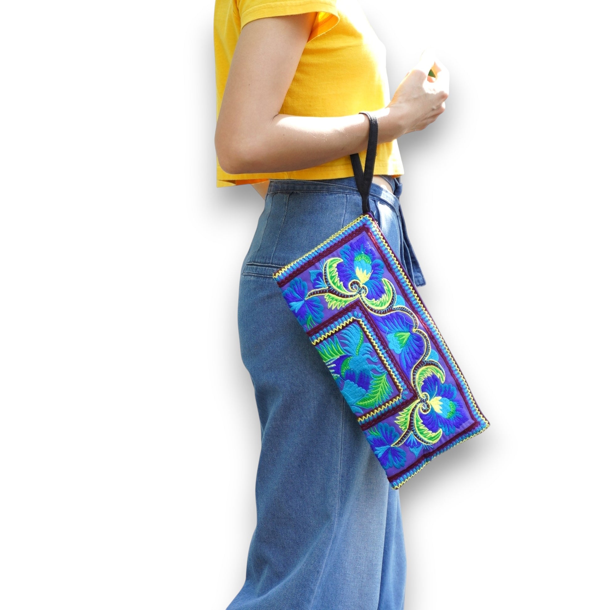 Model holding blue and green peacock wristlet with vibrant Hmong embroidery and bold patterns.