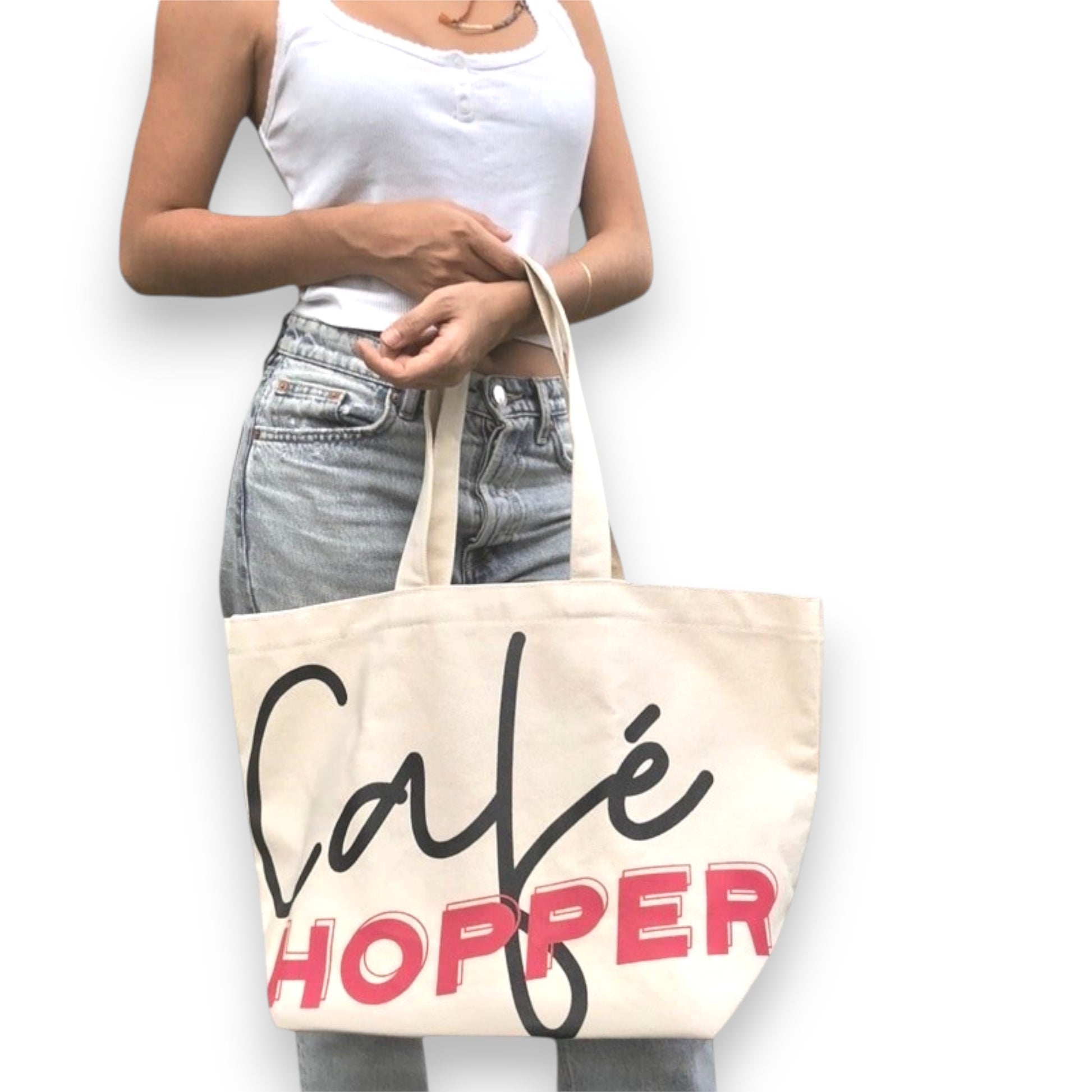 A woman carrying an oversized Café Hopper canvas tote bag with bold lettering.