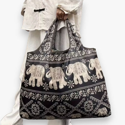 A model carrying a dark brown tote bag with a light brown elephant pattern in their hand.