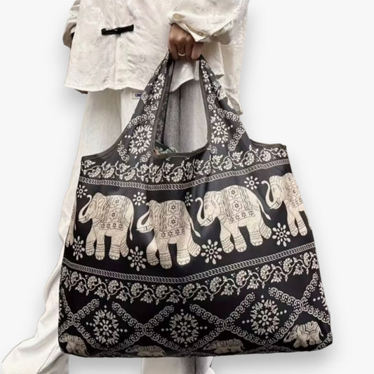 A model carrying a dark brown tote bag with a light brown elephant pattern in their hand.