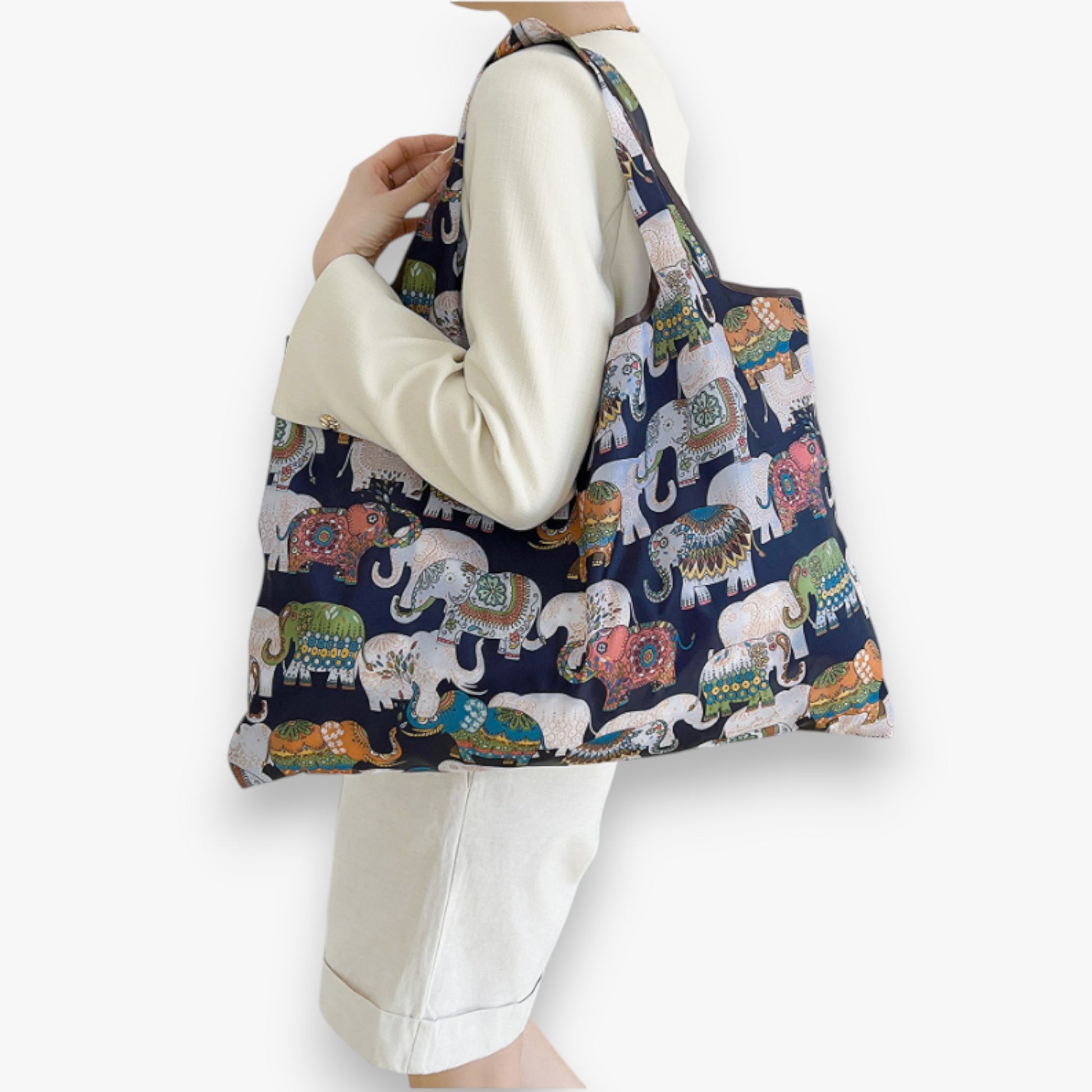 Person holding a navy nylon tote bag with a colourful elephant pattern on their shoulder.