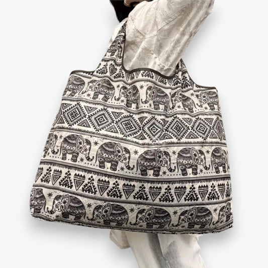 A person carrying a tan shopping tote bag with elephant patterns on the shoulder.