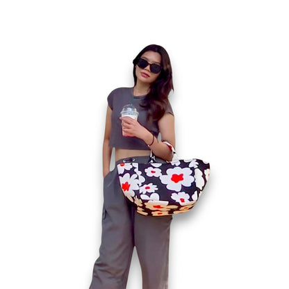 Model holding a large Flower Bomb shopper tote, a black bag with large white flowers, and an orange accent.