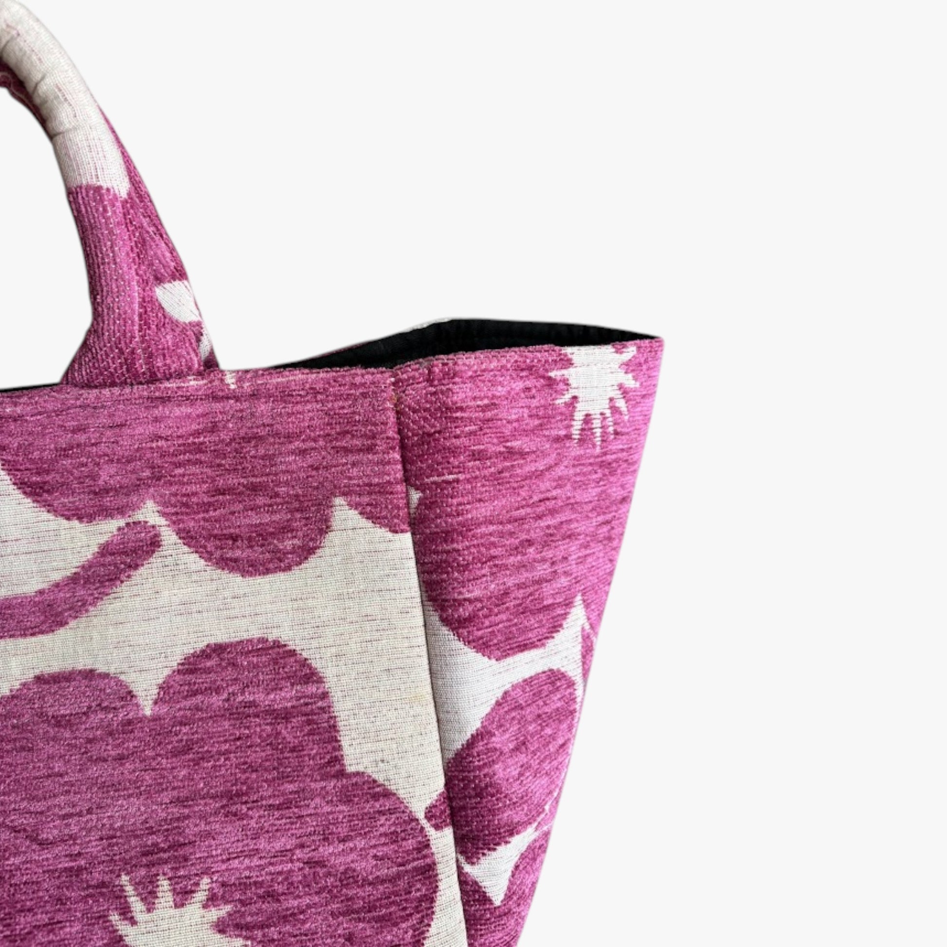 Close-up of a beige fabric with bold magenta floral patterns, displaying a neat handcrafted details.