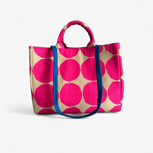 Front view of a hot pink and tan polka dot oversized bag with a contrasting blue strap.