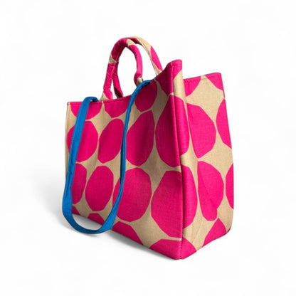 A hot pink and tan polka dot tote bag with a contrasting blue strap in side profile.