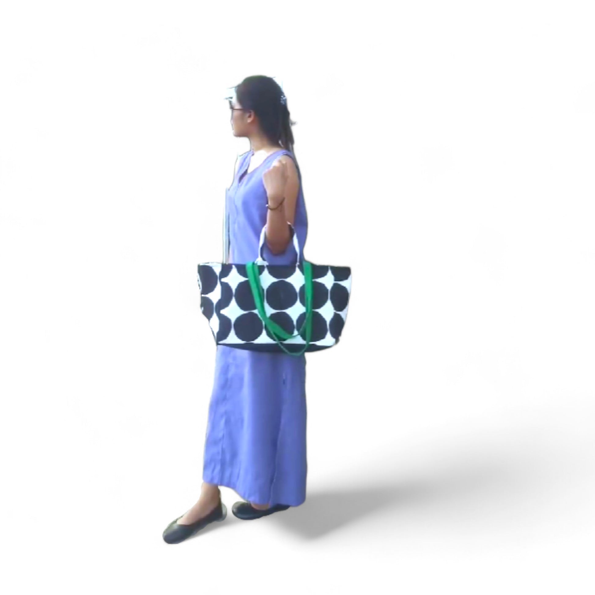 A model carrying an oversized shopper tote with black polka dots and green straps in the crook of her arm.