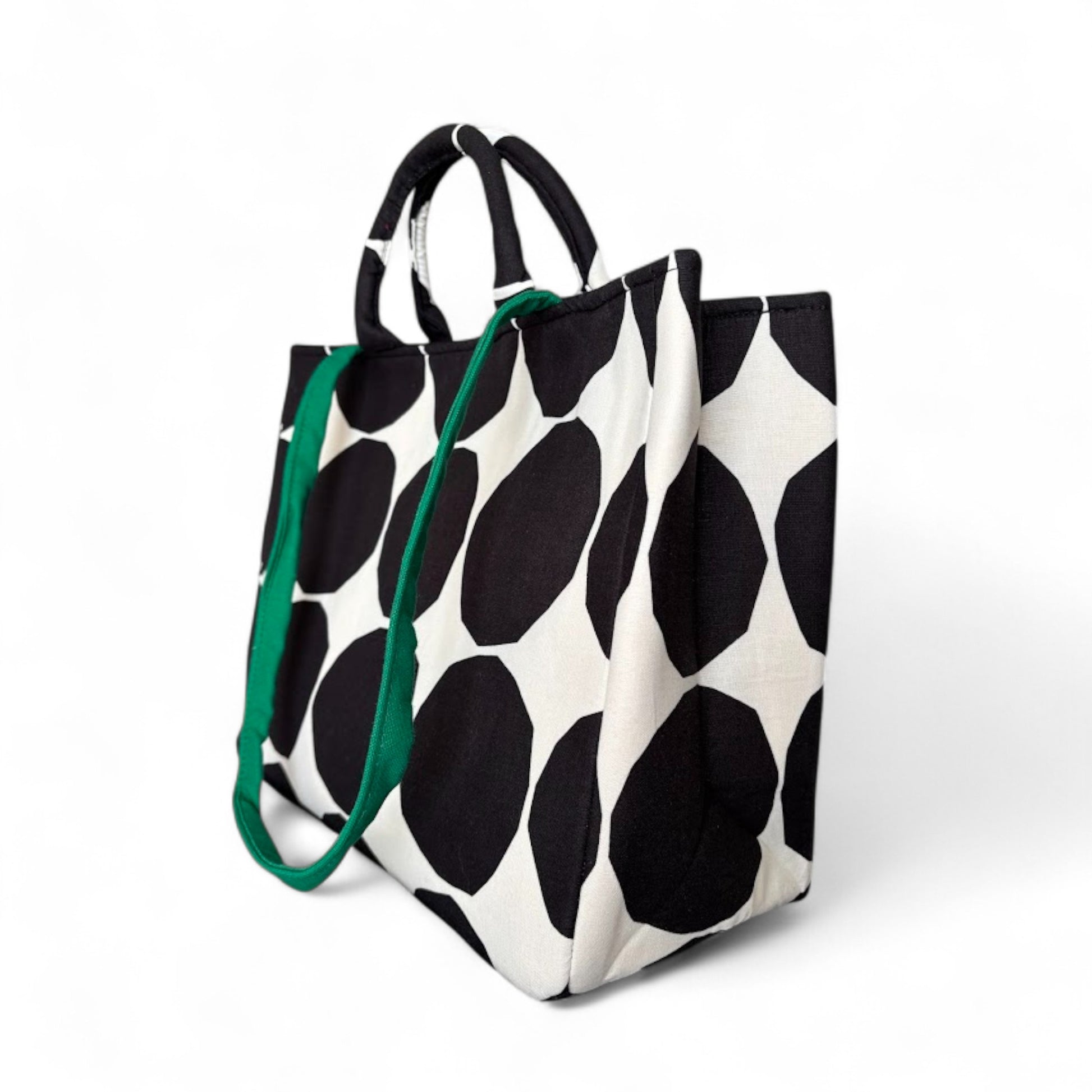 Shopper tote bag with black and white pattern, top handles, and a green strap.
