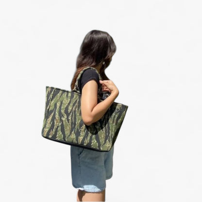 A model carrying a black and green camouflage-patterned tote bag on her shoulder.
