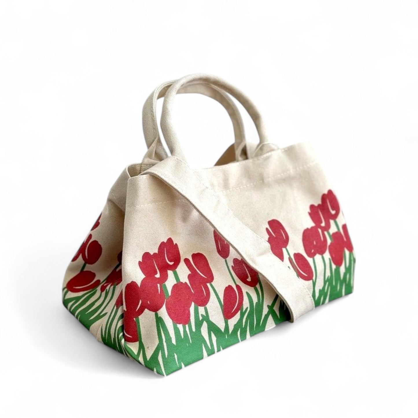 A side view of a canvas shopper tote with red tulip prints, a shoulder trap, and op handles.